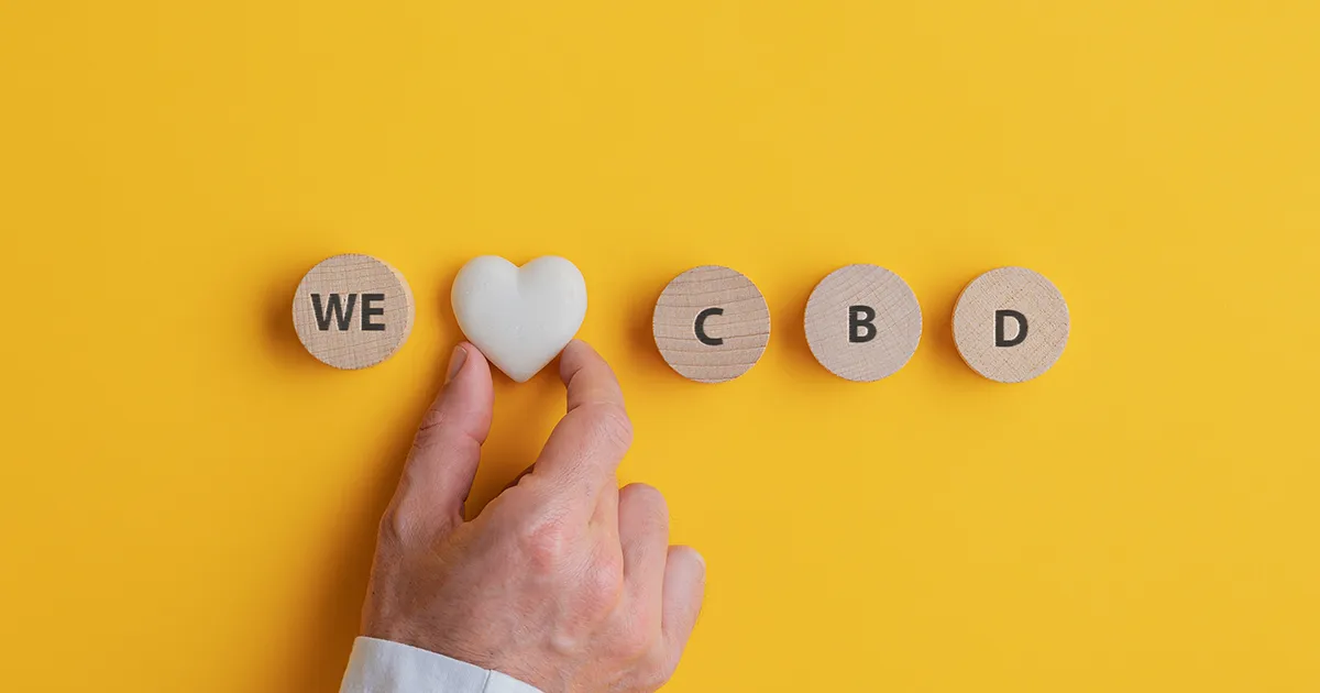 Lettres imprimée sur des petits bois rond disposés pour écrire "We Love CBD". Love est remplacé par un cailloux en forme de cœur. 