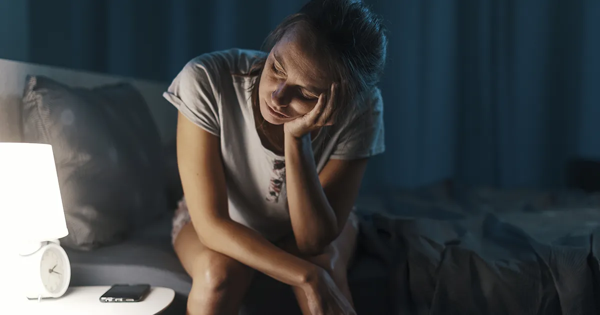 Femme assise sur son lit lampe de chevet allumé lors d'une insomnie.
