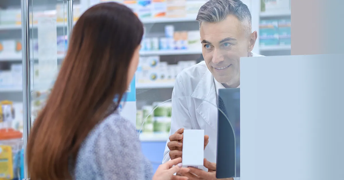 Pharmacien dans une pharmacie derrière le comptoir proposant à un client un produit au CBD.
